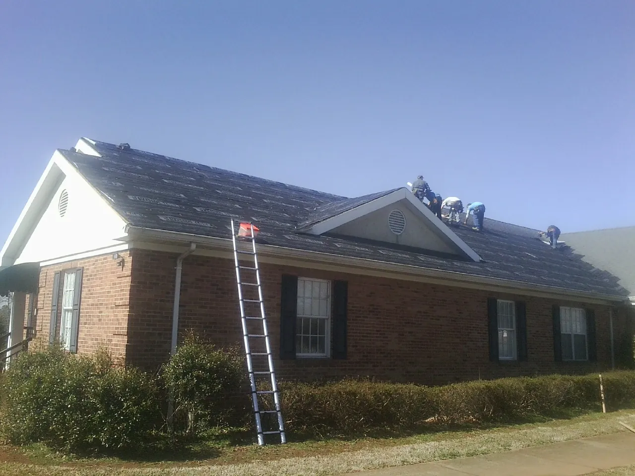 Crew tearing shingles off a brick ranch roof with a ladder set — Metal Roof Repair work by our crew in Waukesha