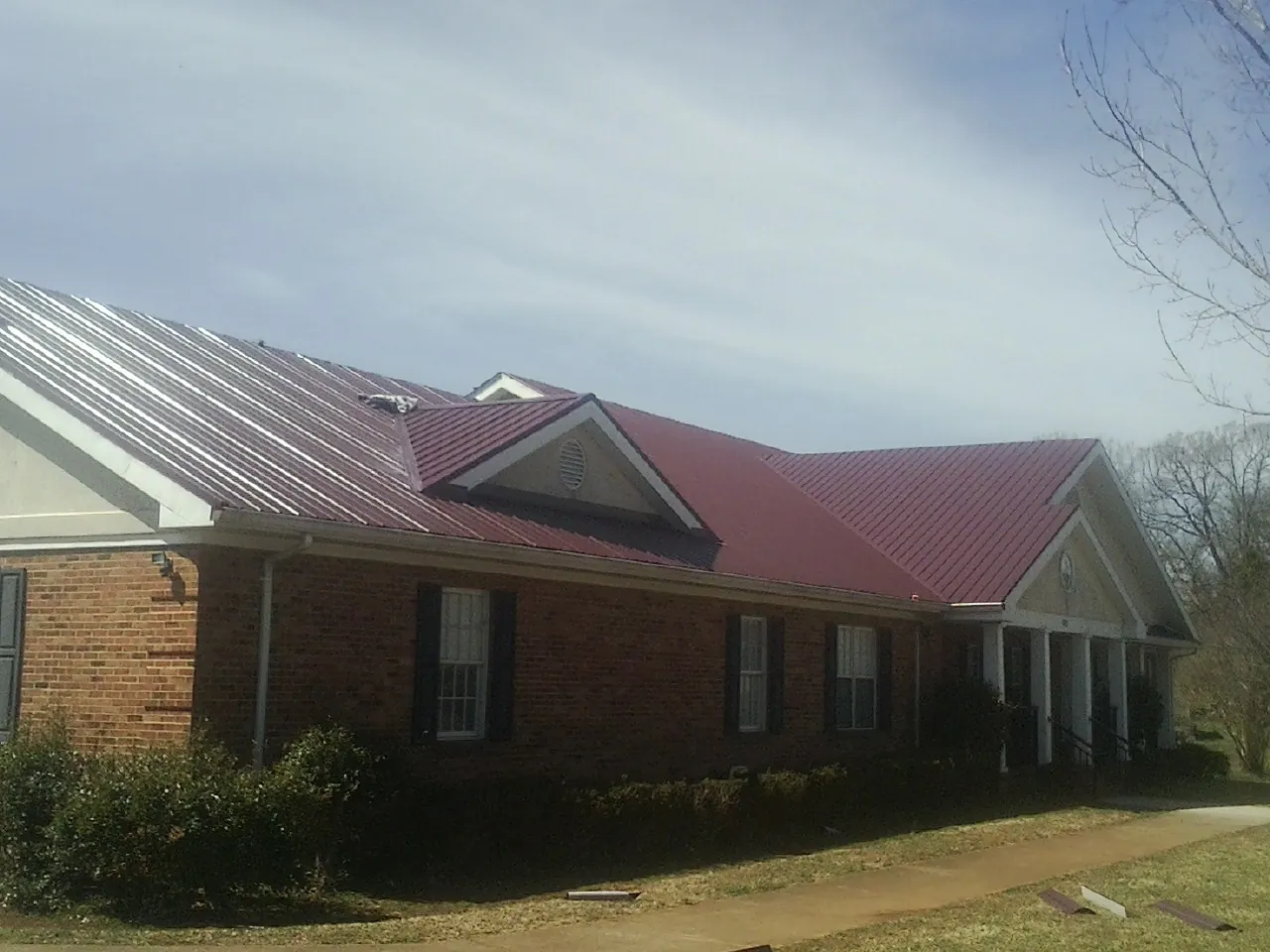 Red metal roof with gabled entries on a long brick building, from a Hail Damage Roof Repair job in Waukesha