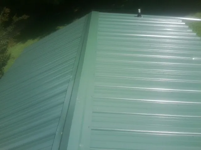 New green metal panels meeting at the ridge of a roof — Flat Roof Repair work by our crew in Waukesha