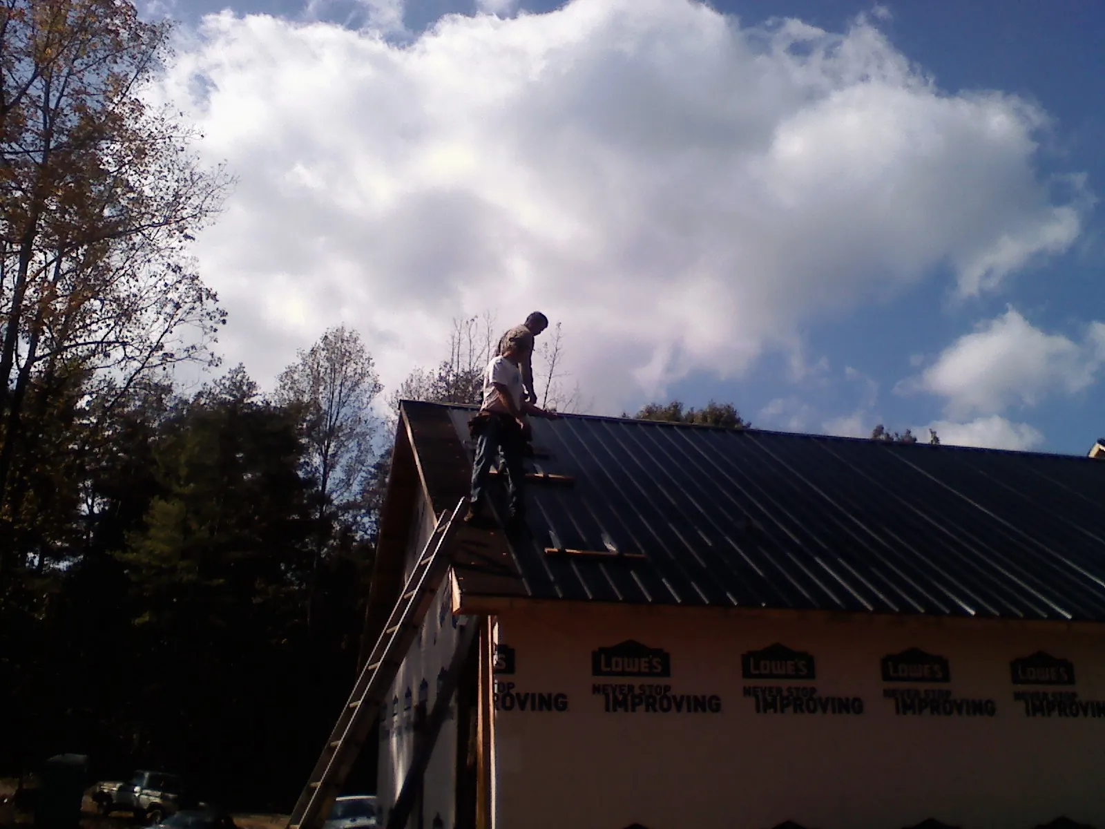Roofer fastening dark metal panels high against a cloudy sky, from a Roof Inspection job in Waukesha