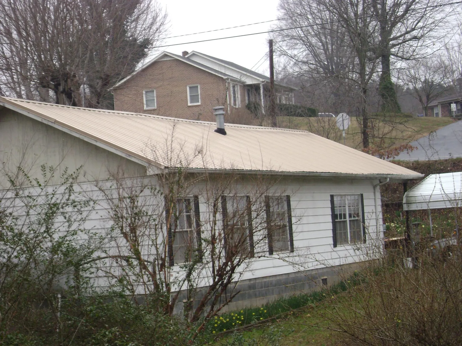 Tan metal roof on a white sided house set into a hillside — Commercial Roofing by Roofing Brothers in Waukesha
